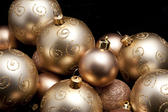Pile of different luxurious golden Christmas balls with patterns and textures against a dark background with copyspace
